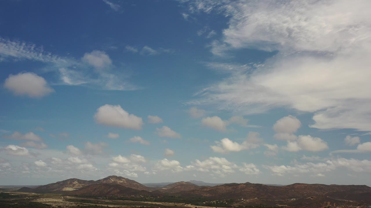 Wide blue sky over low brown mountains and green terrain.