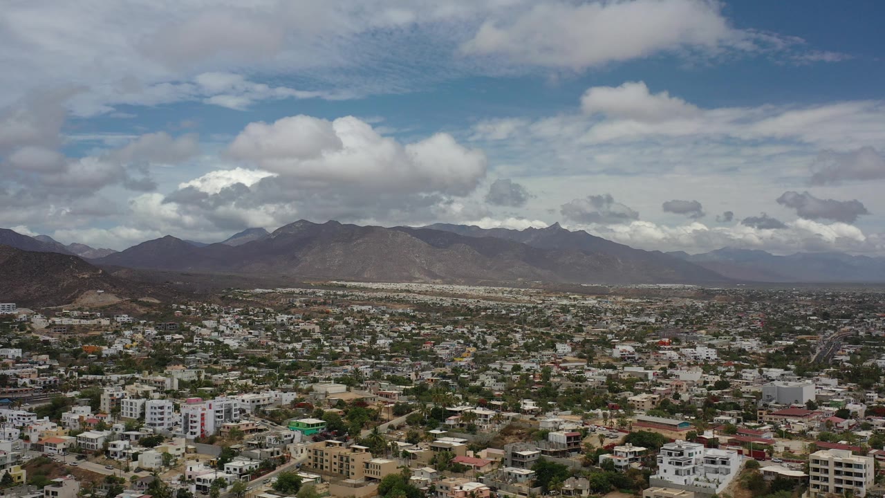 Aerial view of a low-rise city below cloudy sky and distant mountains.