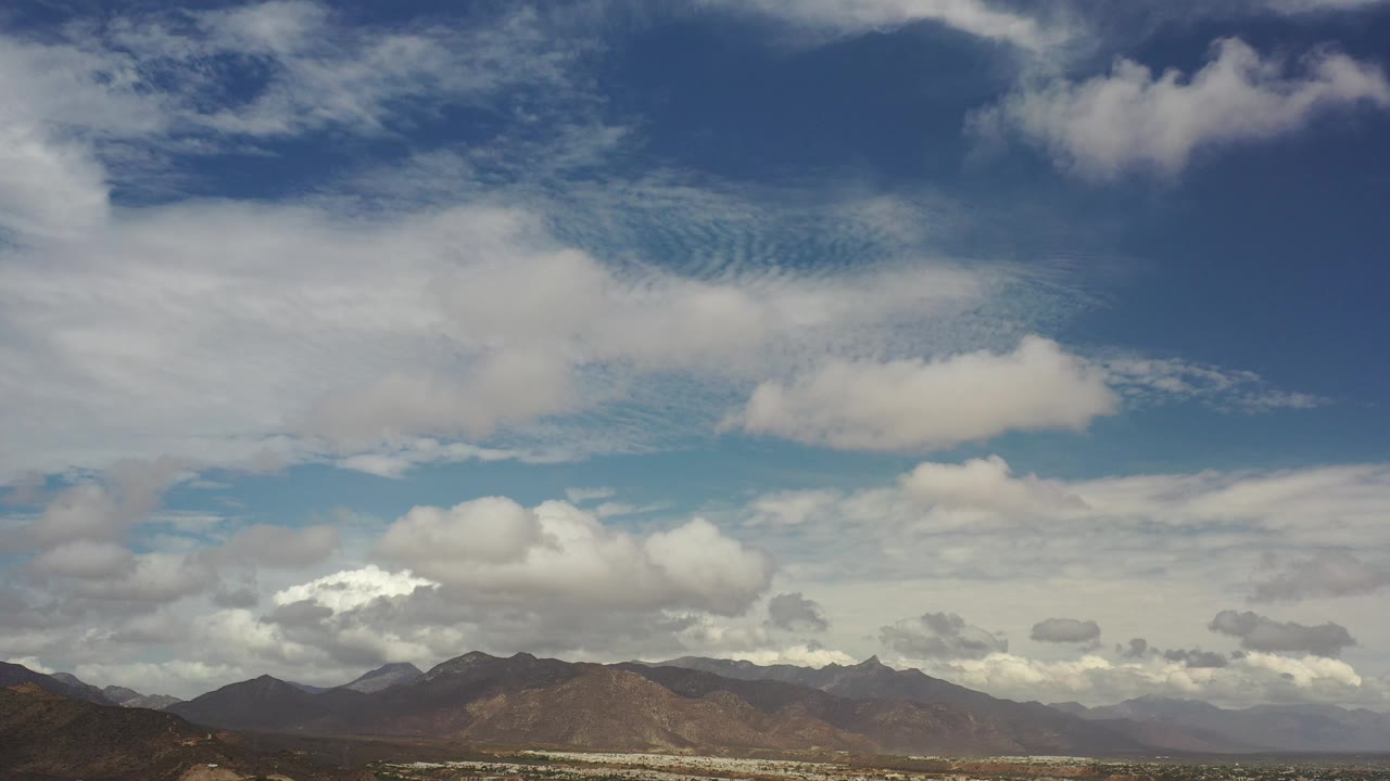 Distant mountains under layered white clouds and blue sky.