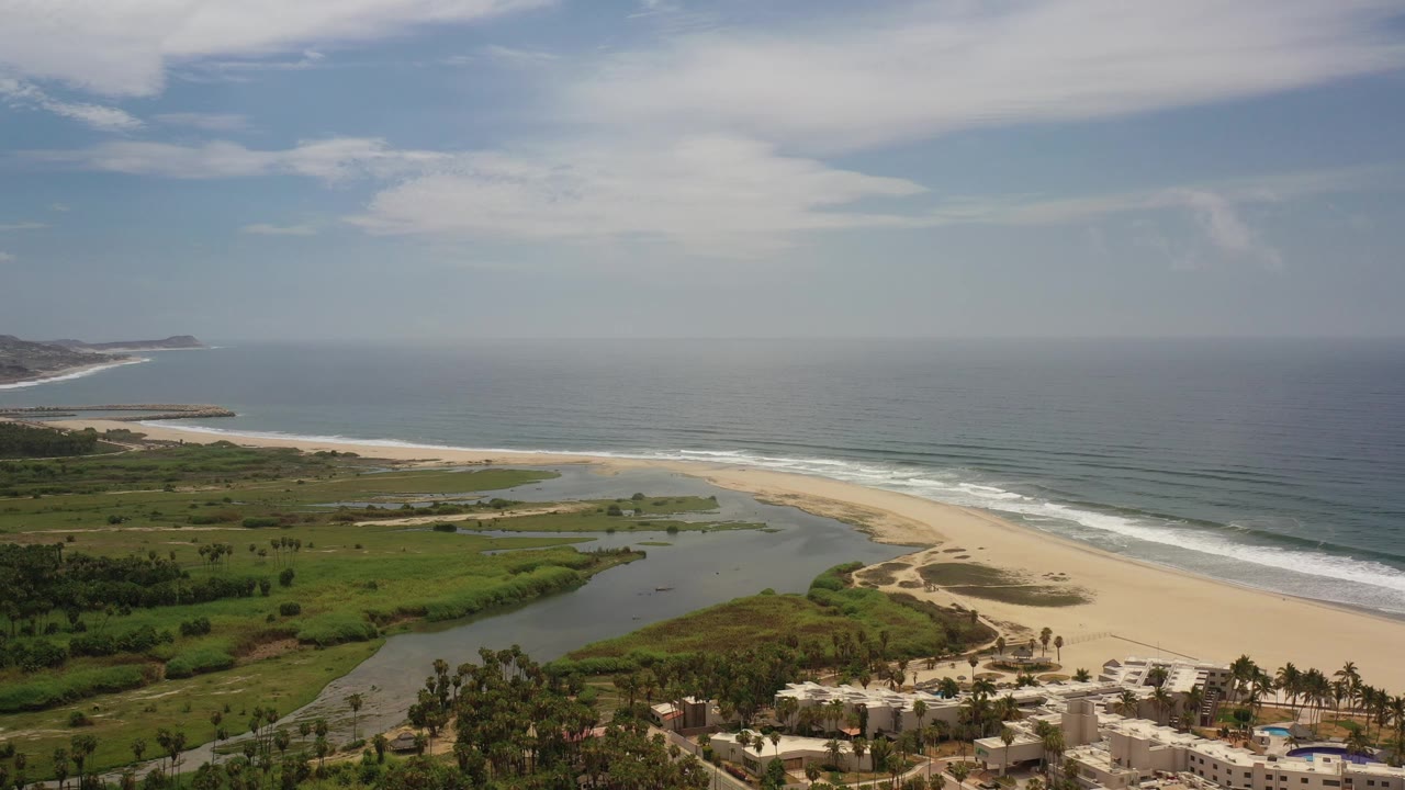 Aerial view of sandy beach, green coastal land, and blue ocean.