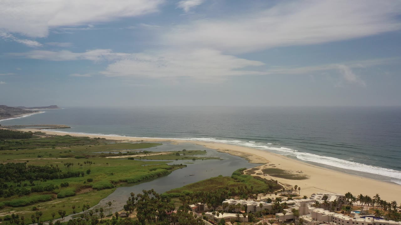 Wide aerial coastline with beach, lagoon, greenery, ocean, and sky.