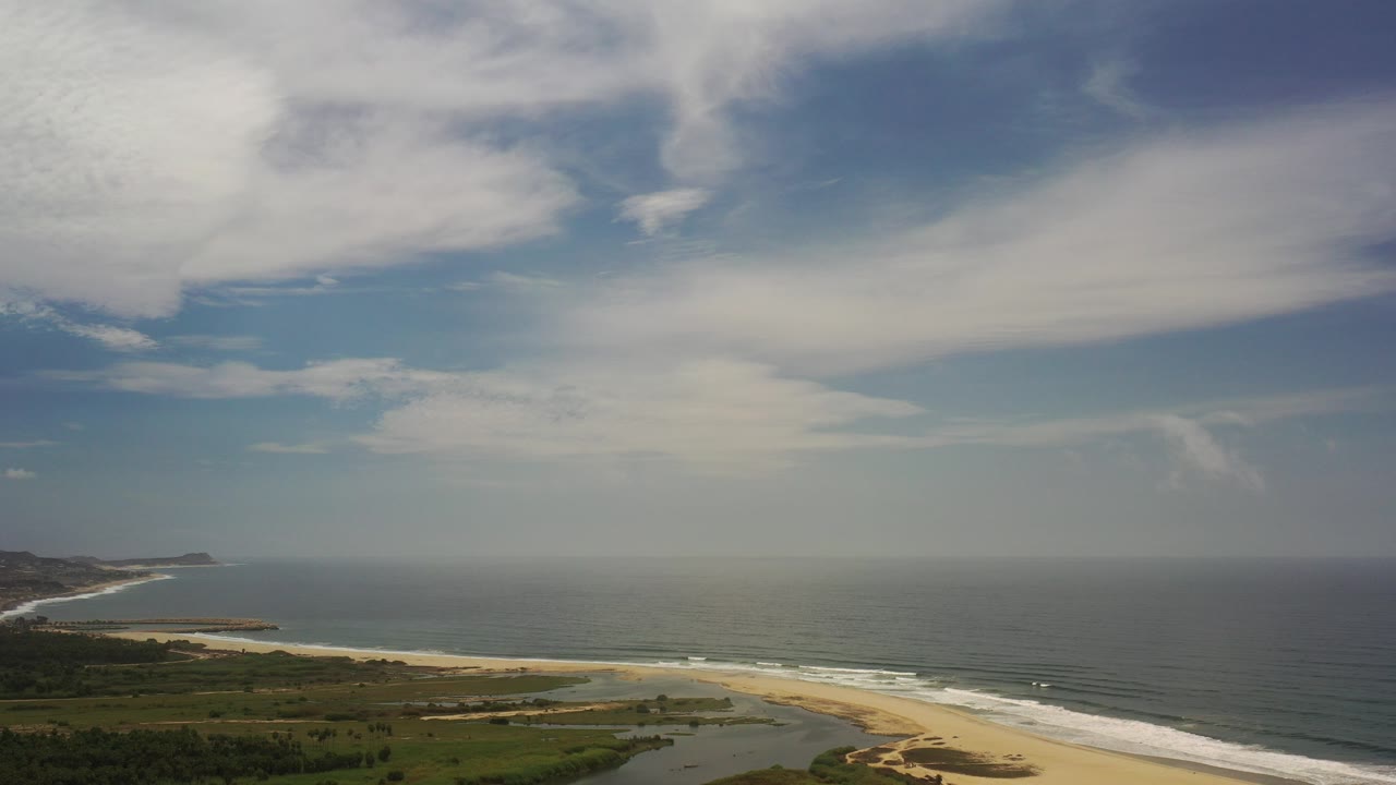 Opening frame of a Los Cabos, Mexico aerial view with broad cloud cover above the ocean, a sandy beach below, and no visible people.