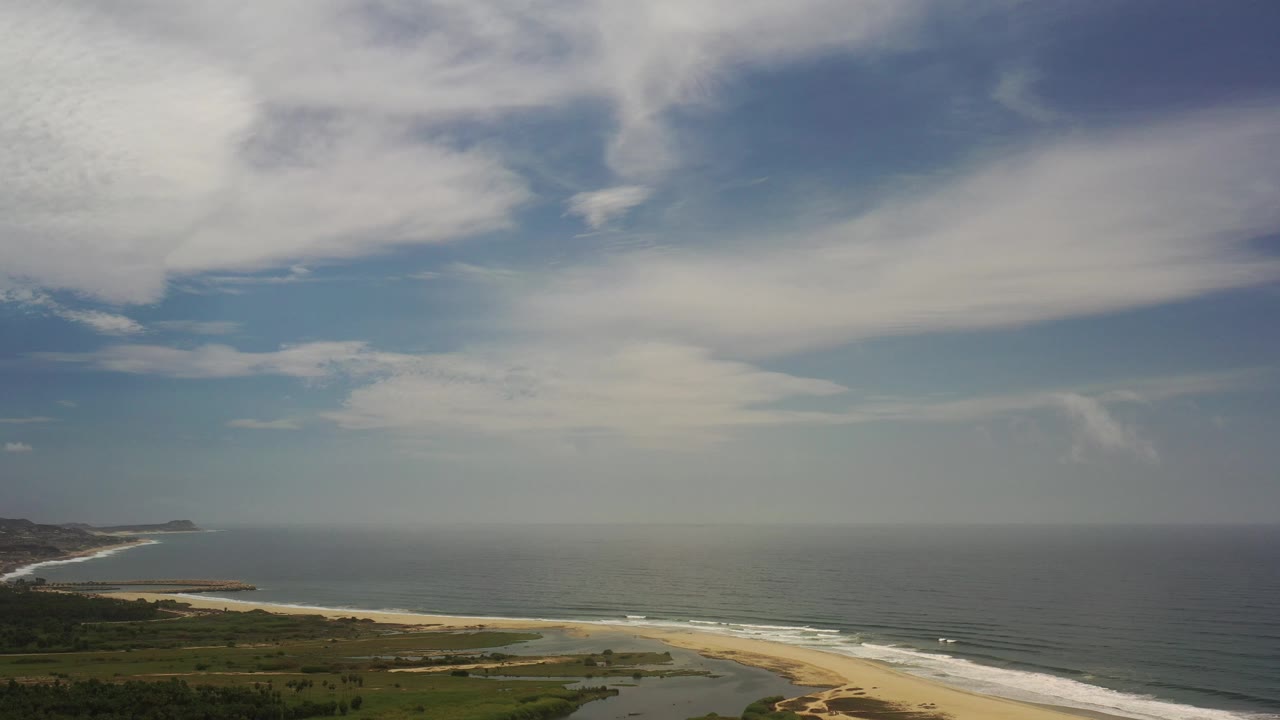 Cloud-filled sky over hazy ocean and a curving sandy beach.