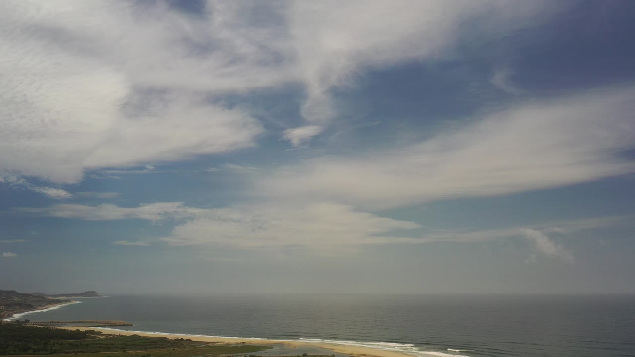 Cloudy sky over ocean and sandy coastline.