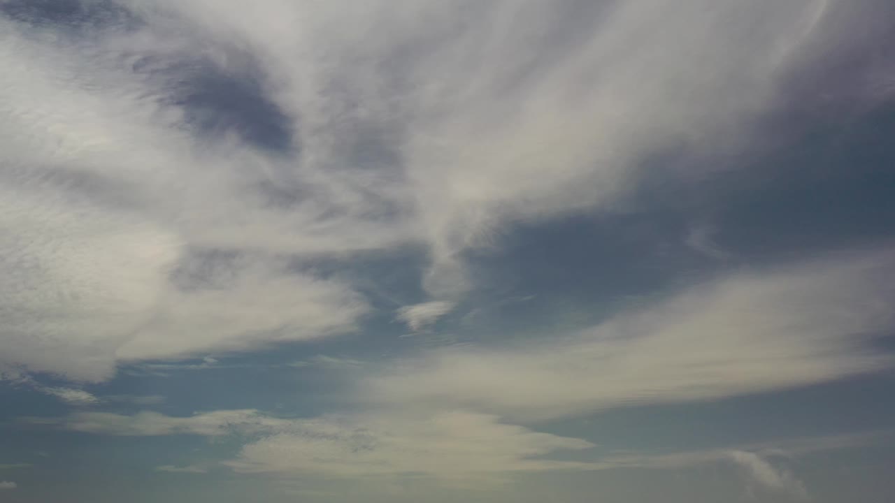 Thin cloud layers cover most of the pale blue sky in Los Cabos, with a darker blue opening near the upper left and no visible people.
