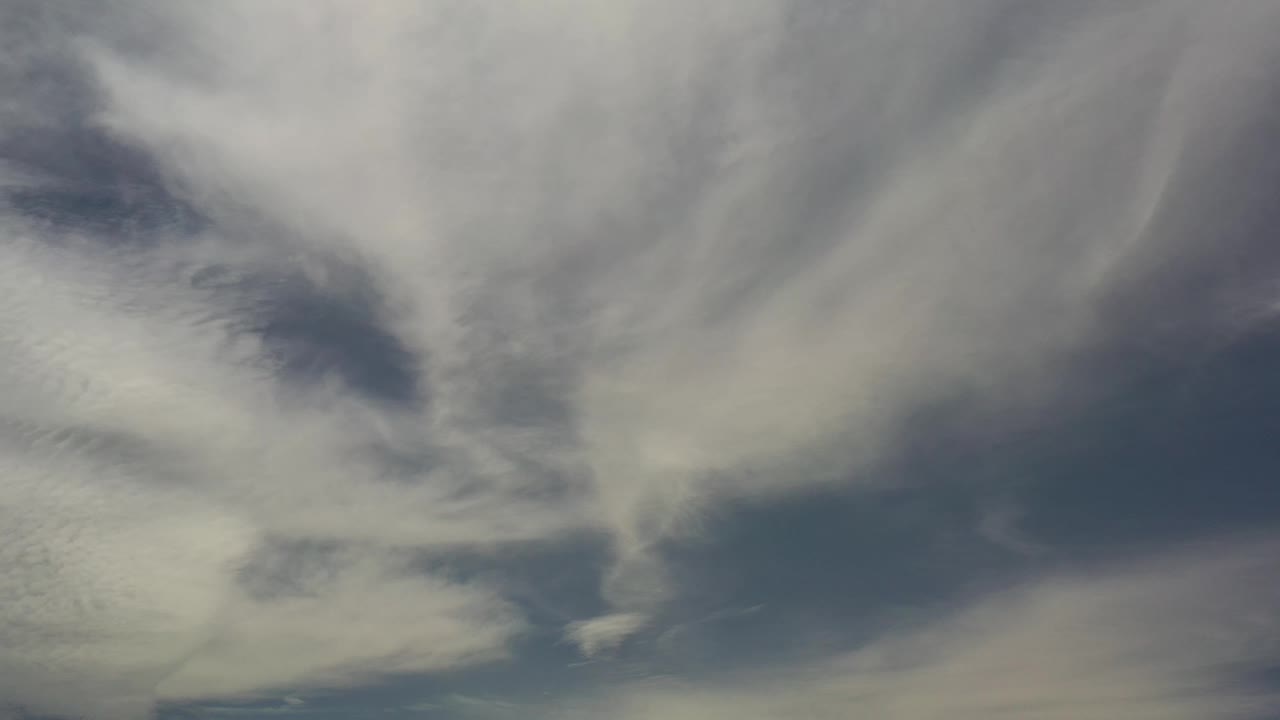 Pale layered clouds drift across a darker blue opening in the Los Cabos sky, with no ground or visible people.