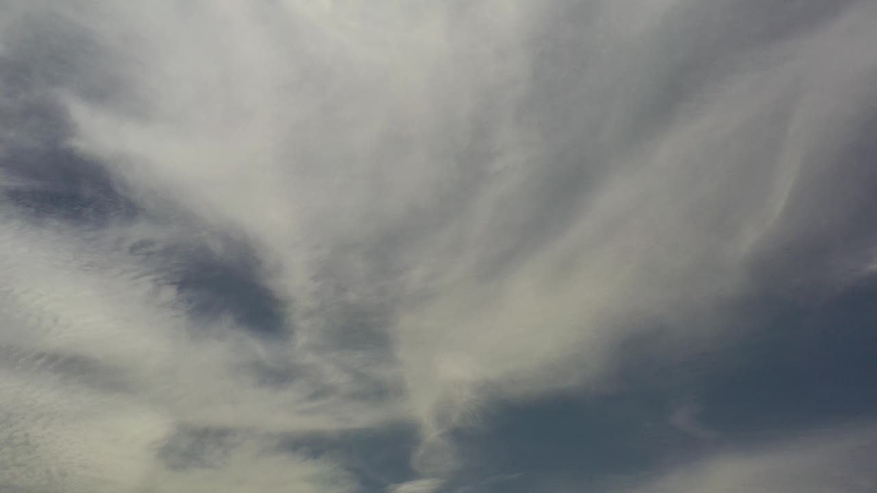 Soft white and gray cloud bands fill the Los Cabos, Mexico sky at the start of the clip, with darker blue openings and no visible people.