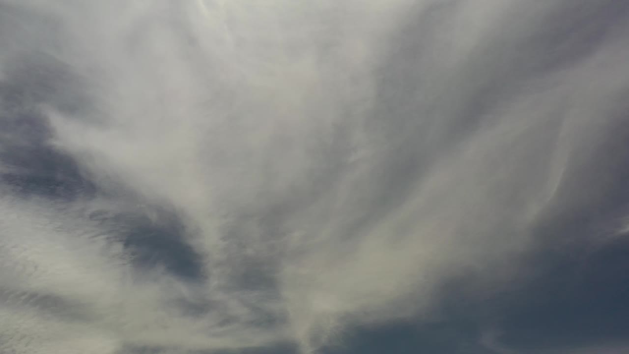 Cloud bands stretch diagonally through the frame over Los Cabos, Mexico, with muted blue sky visible between the pale white and gray forms.