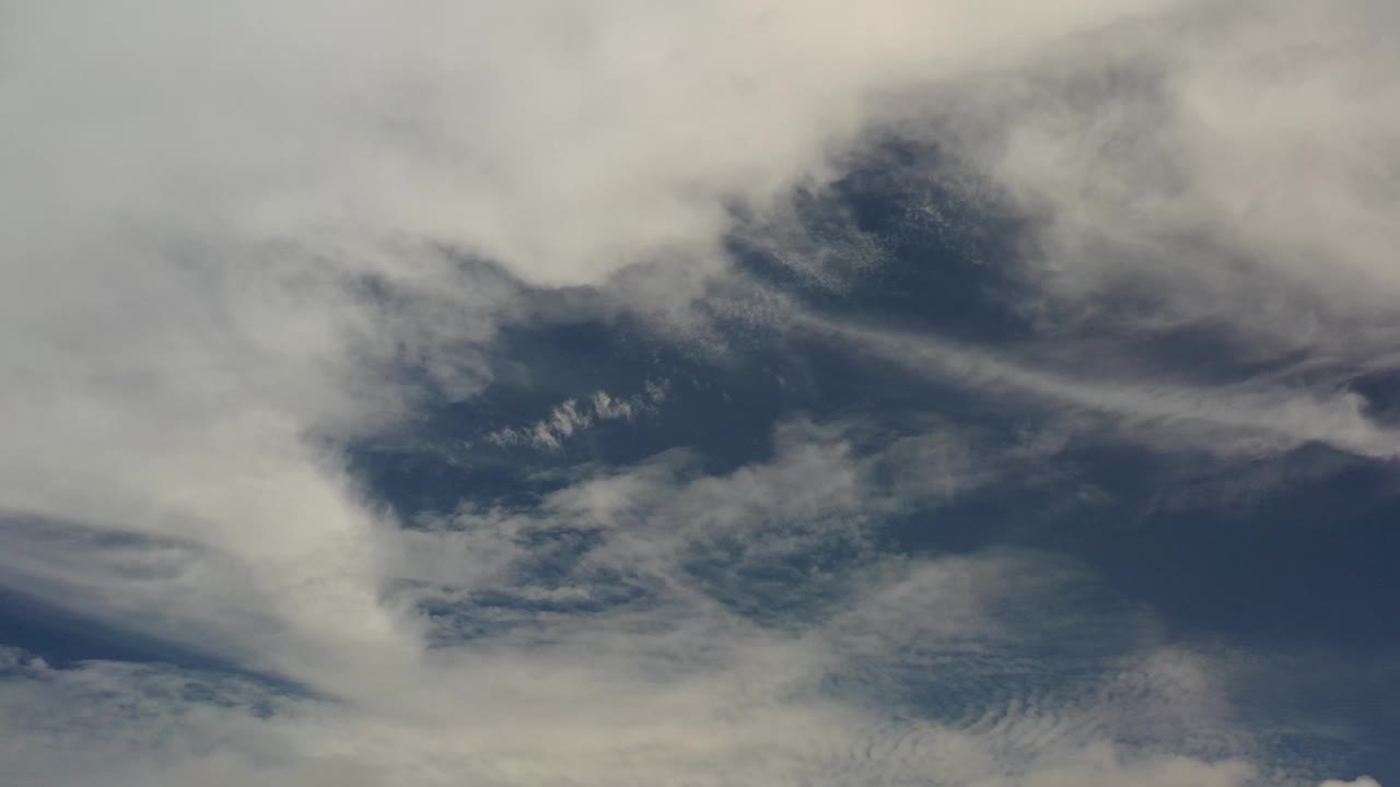 Early frame from Los Cabos with a broad pale cloud mass at the top and darker blue sky showing through the center, with no visible people.