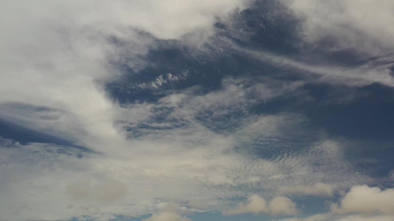 Early frame showing streaked cloud layers and a darker blue-gray cloud patch high in the Los Cabos sky, with no visible people.