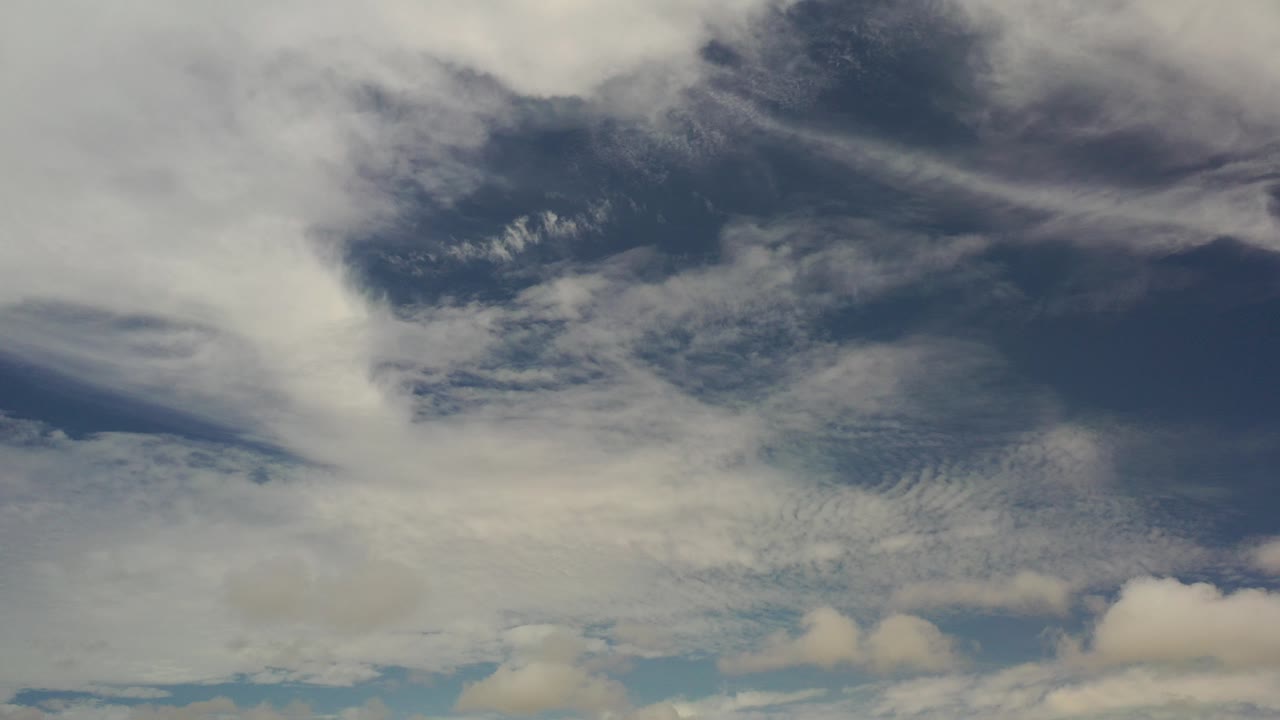 Opening frame of layered white and gray clouds over blue sky in Los Cabos, Mexico, with no visible people.