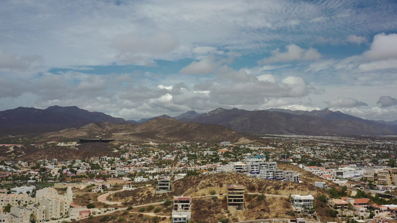 Wide aerial view of hills, buildings, mountains, and clouds.