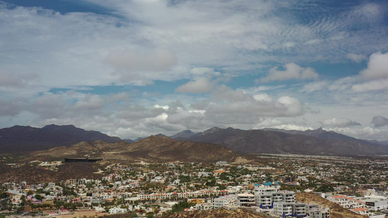 Wide aerial view of a city below hills and a cloudy sky.