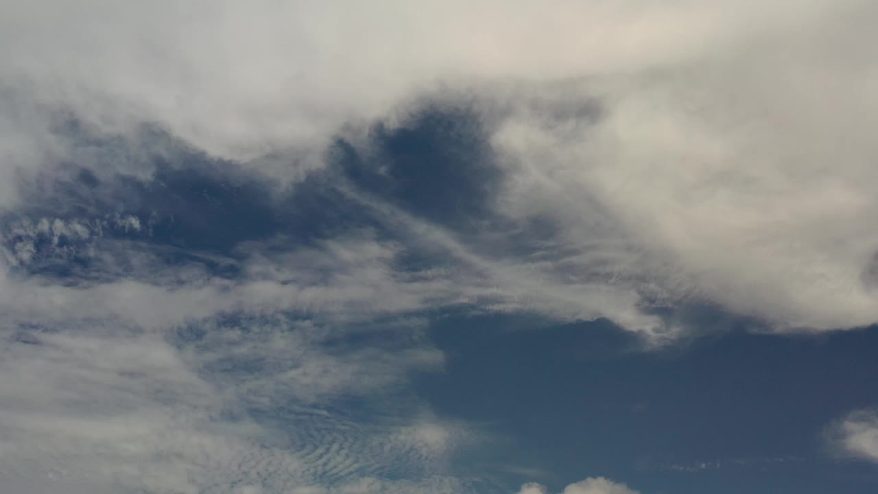 A dense white cloud mass sits near the top of the Los Cabos sky while thinner streaks cross the blue center, with no visible people.