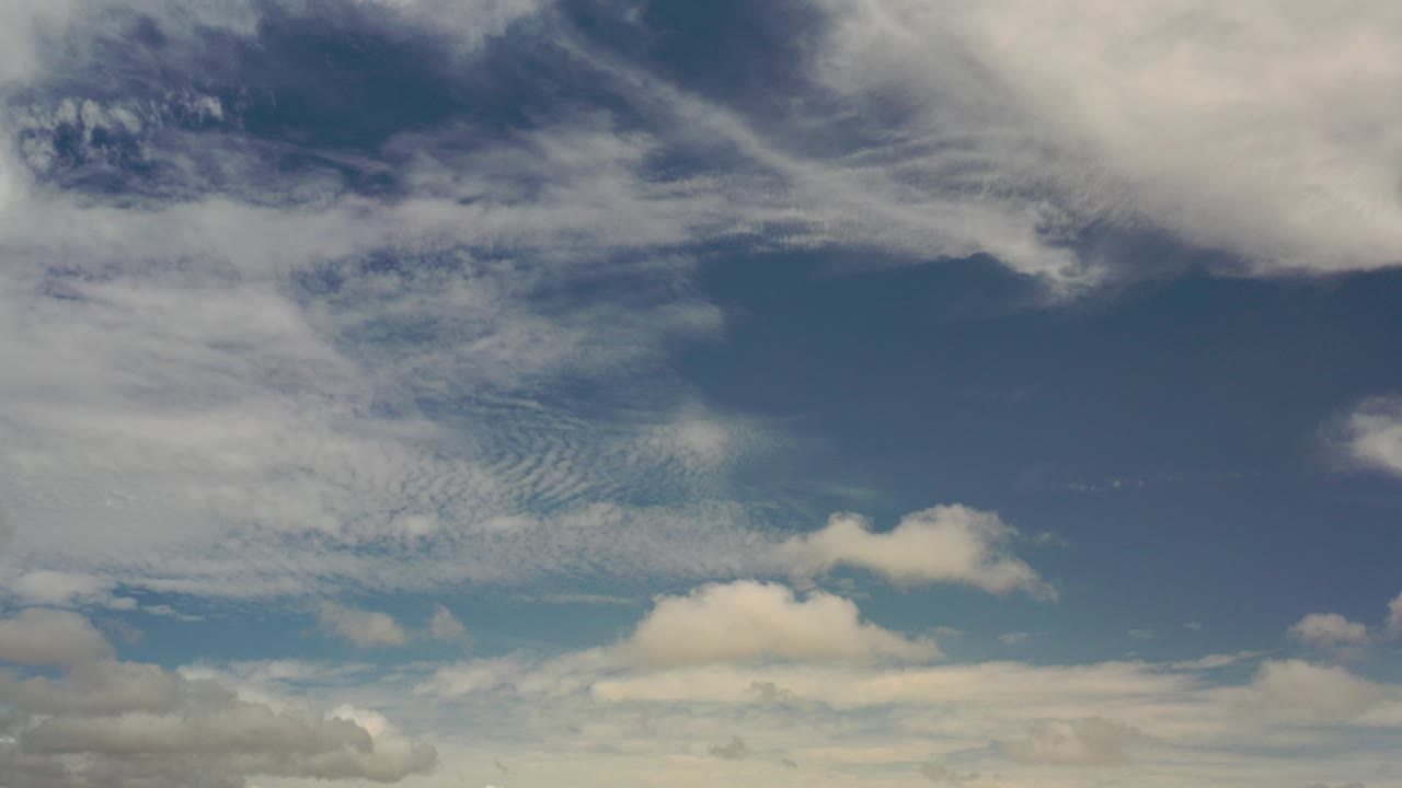 Opening frame of a blue Los Cabos sky filled with white and gray cloud layers, with only a faint low horizon and no visible people.