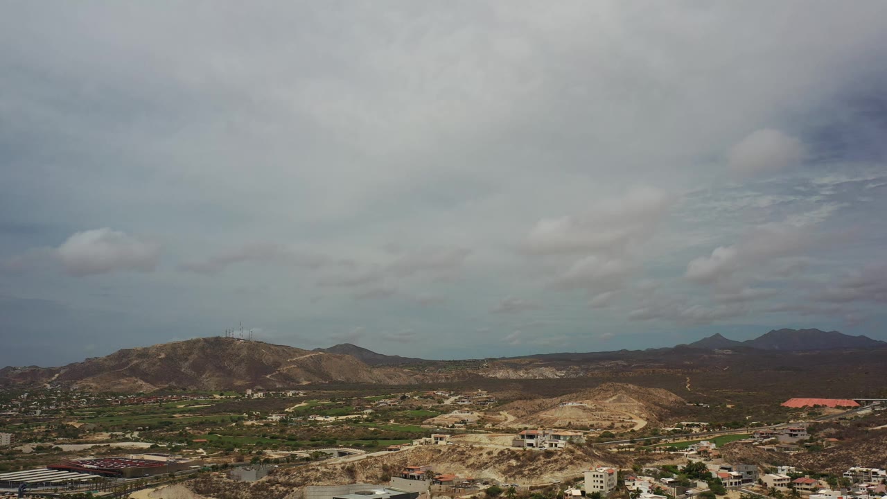 Los Cabos aerial landscape with a low mountain ridge on the left, darker distant hills, foreground buildings, and no visible people.