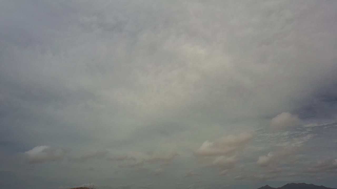 Dense overcast clouds fill most of the Los Cabos frame above faint distant hills, with no visible people.