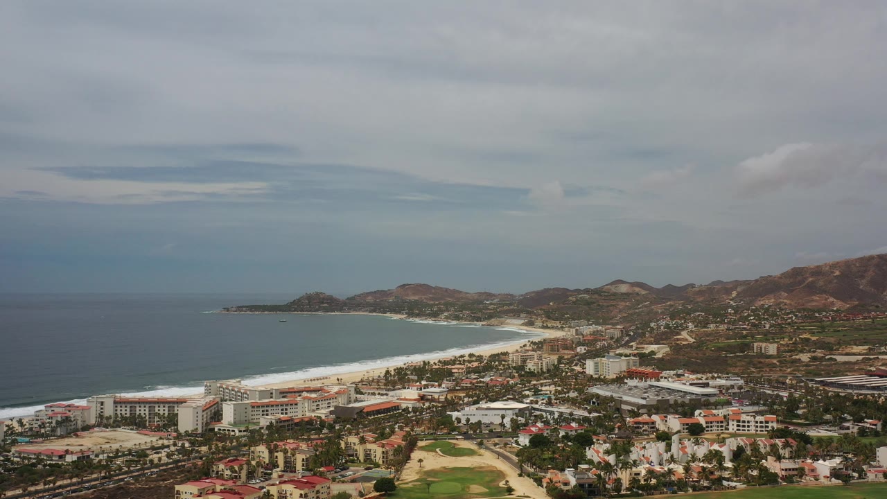 Beach town aerial with ocean, white surf, and hills