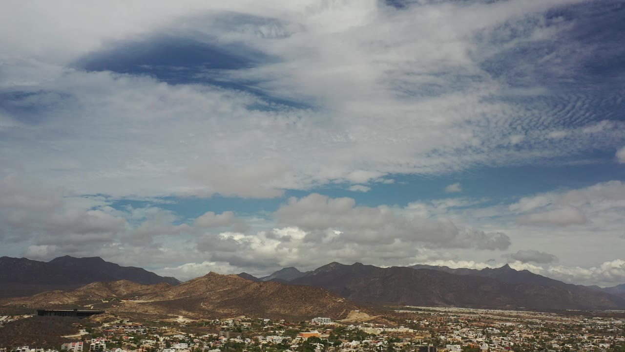 Opening view of Los Cabos, Mexico, with brown mountain ridges below a broad cloud-filled sky and no visible people.