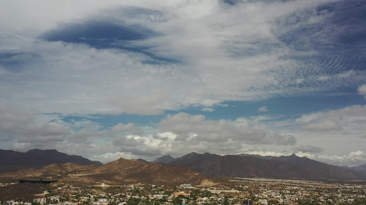 Brown hills and darker mountains below a textured cloudy sky.