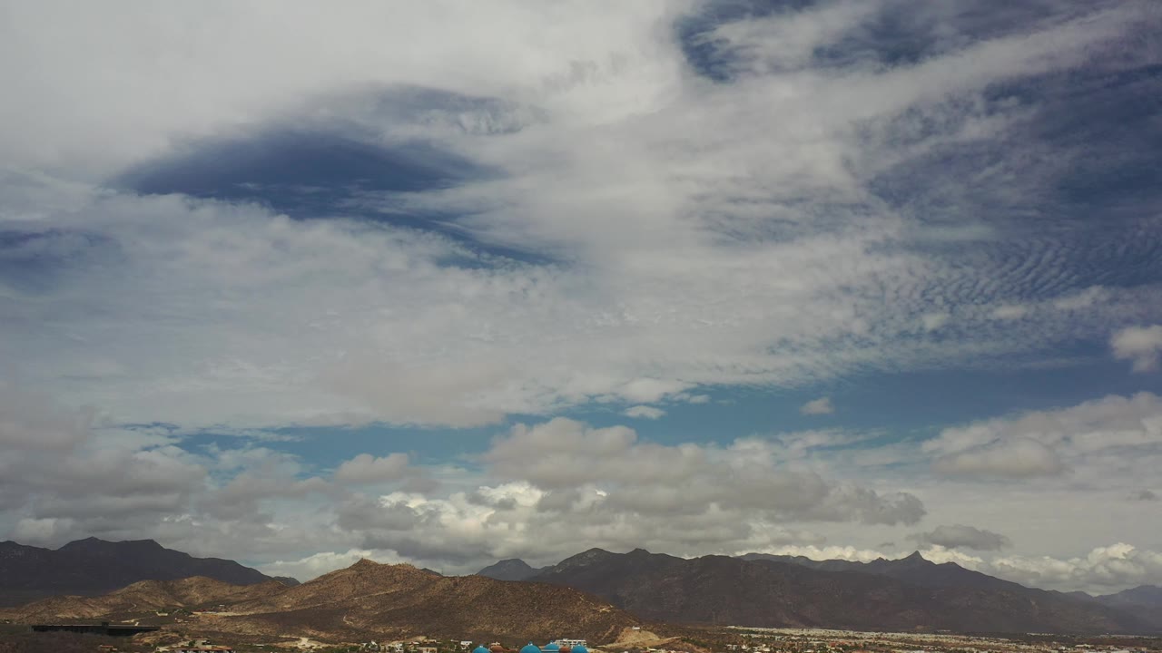Cloud-filled sky over tan and dark ridgelines