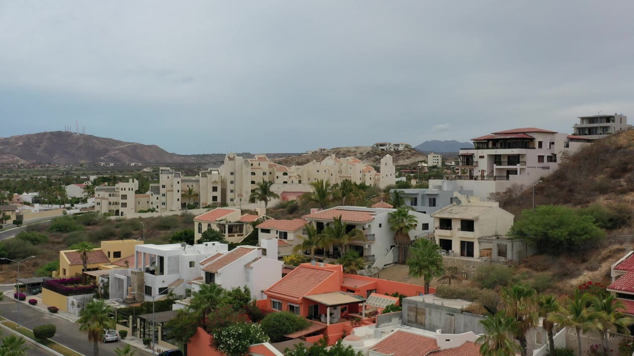 Elevated view of hillside homes, rooftops, and mountains under a gray sky.