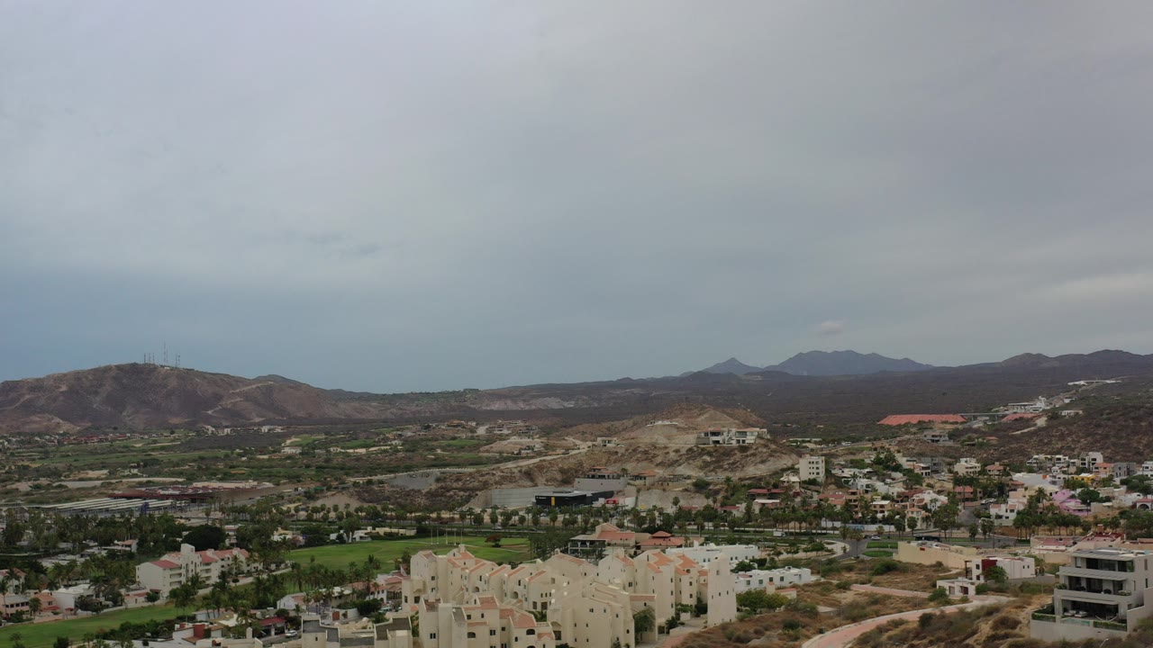 Wide aerial view of hills, valley buildings, and cloudy sky.