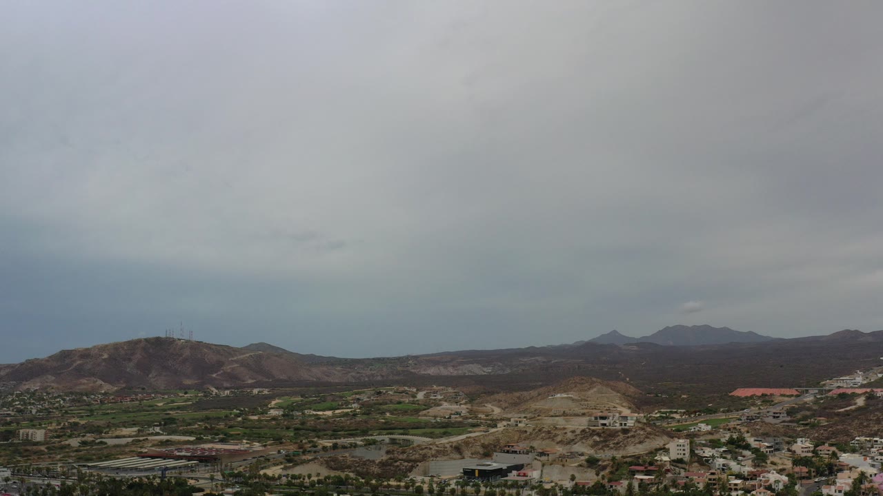 Wide cloudy view over hills, valley, and distant mountains.