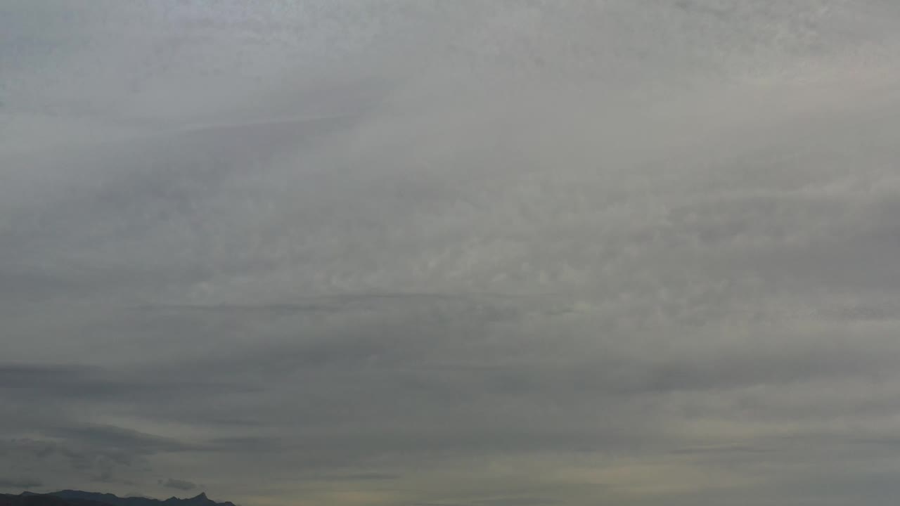 At 0:01, layered gray clouds hang over dark Los Cabos mountains with a faint low horizon and no visible people.