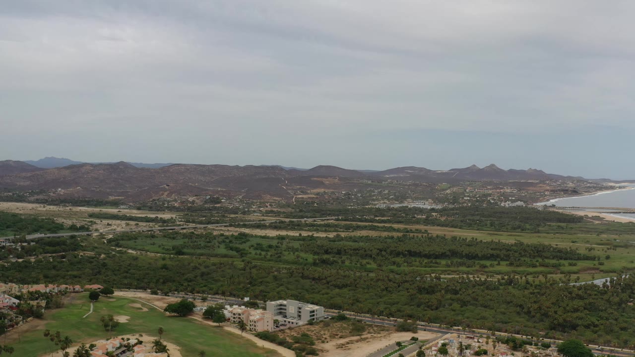 Second frame shows the Los Cabos landscape from above, with low buildings near the foreground, green terrain across the middle, distant hills, coastline, and no visible people.