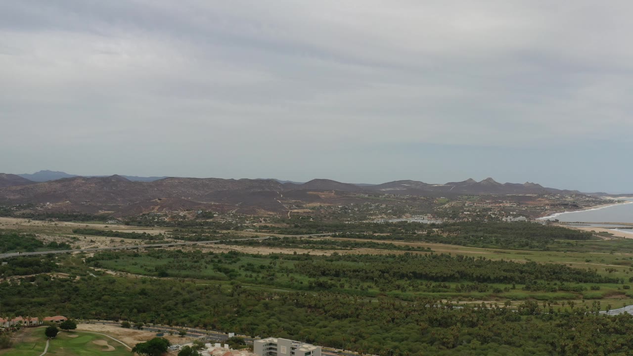 Green pastures and trees below rolling hills with a pale bay in the distance.