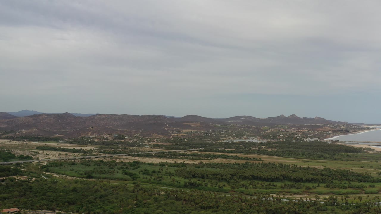 Wide view of green plains, brown hills, coastline, and cloudy sky.