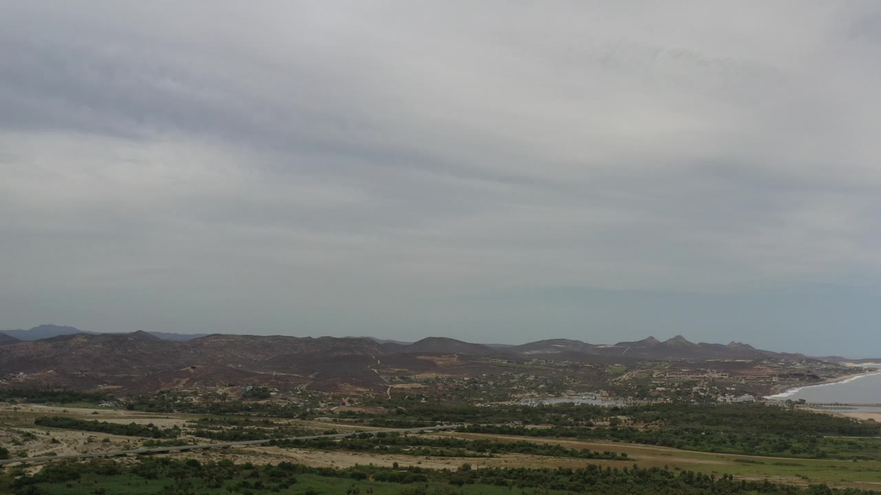 Aerial view of brown hills, green vegetation, and gray clouds