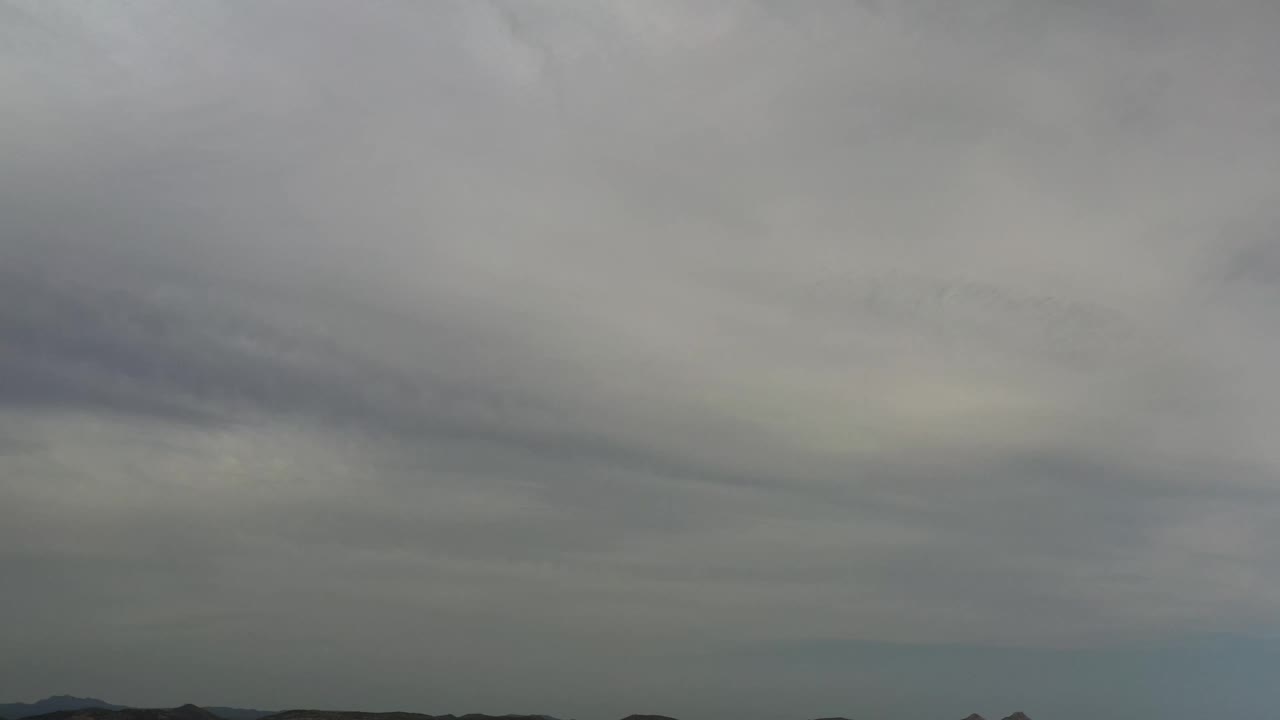 A heavy cloud ceiling remains over the Los Cabos horizon, with muted light and no visible people.
