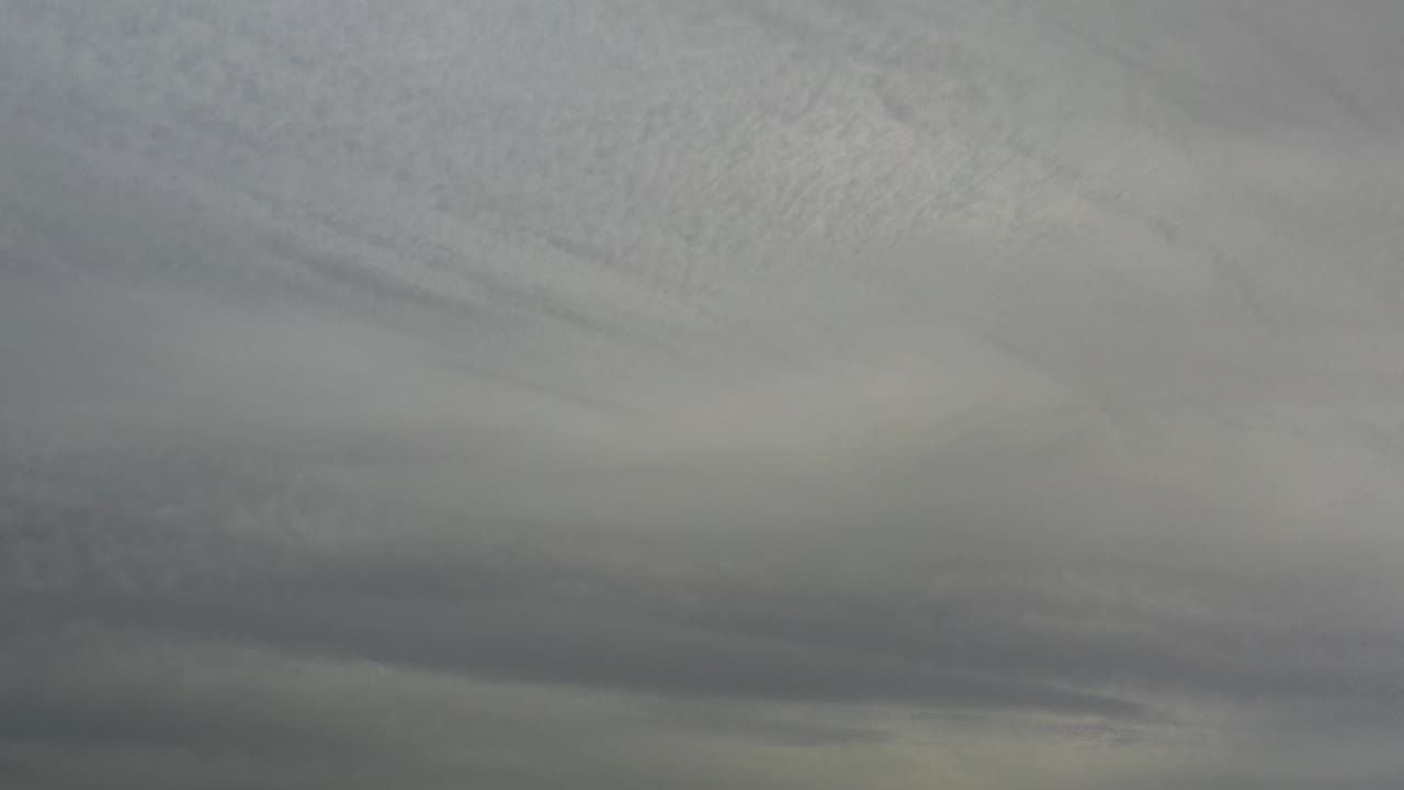 Dense gray cloud layers fill the frame over Los Cabos, Mexico, with darker bands low in the image and no visible people.