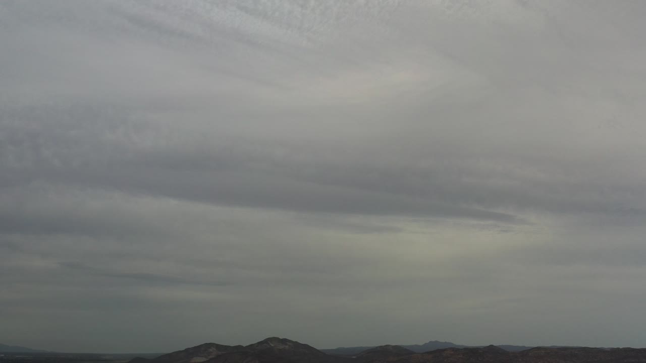 Wide overcast view in Los Cabos, Mexico, with a thick gray cloud layer above low mountain ridges and no visible people.