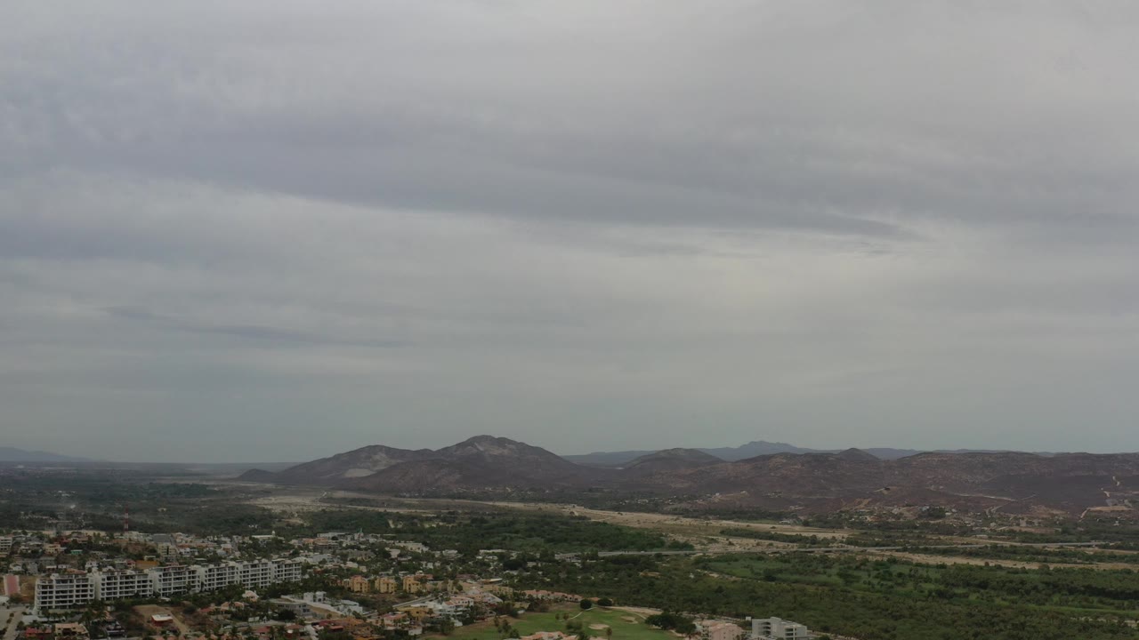 Aerial city edge below mountains and heavy gray sky.