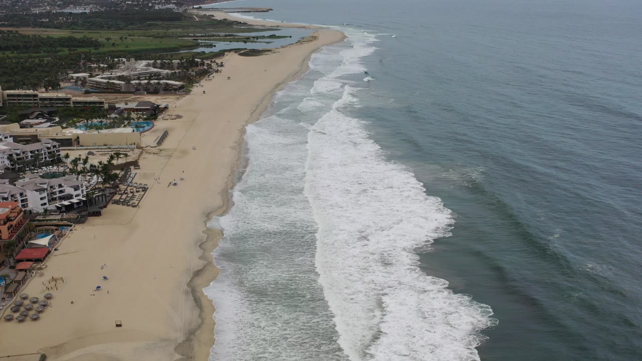 Aerial view of sandy beach, surf, ocean, and beachfront buildings.