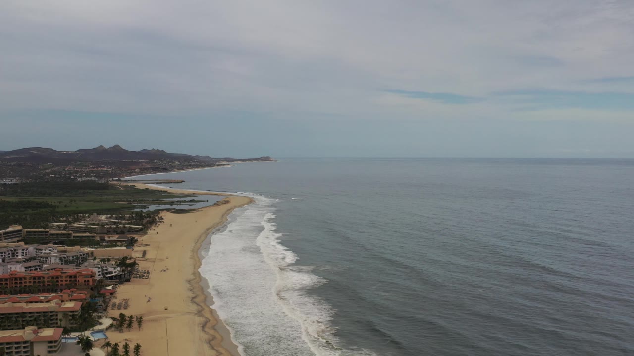 Beach coastline seen from above with waves, ocean, clouds, and hills.
