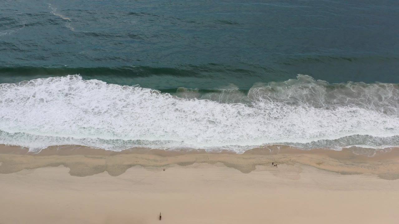Overhead view of waves breaking onto a sandy beach.
