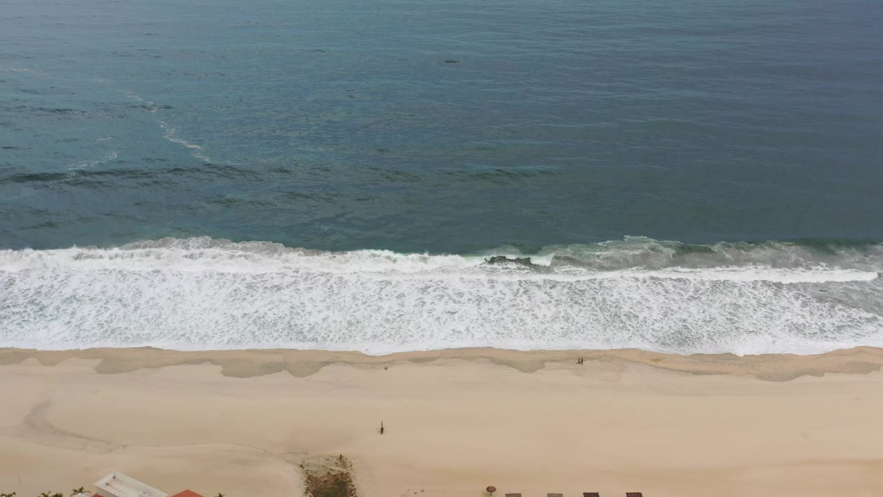 Overhead Los Cabos beach frame with a wide band of white water, darker wet sand scallops, pale dry sand, and no visible people.