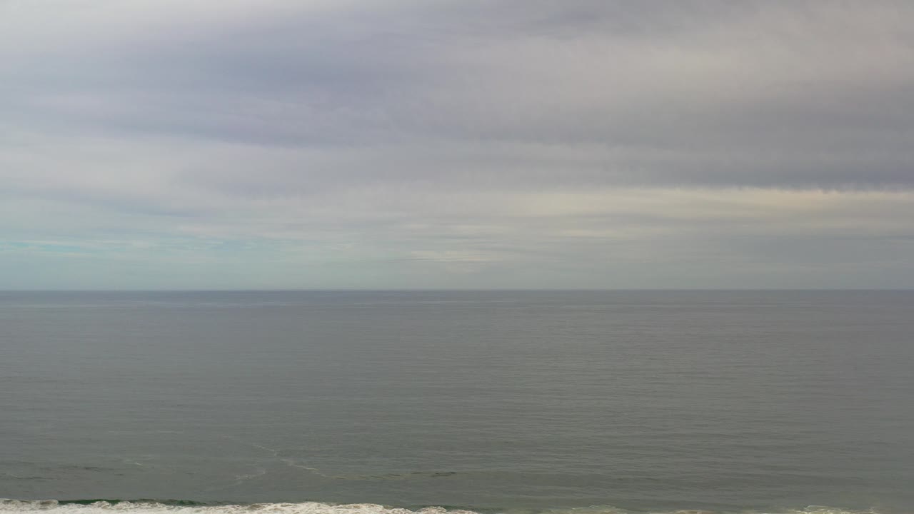 Wide Los Cabos ocean view at the start of the clip, with gray water, a straight horizon, dark cloud bands, and no visible people.
