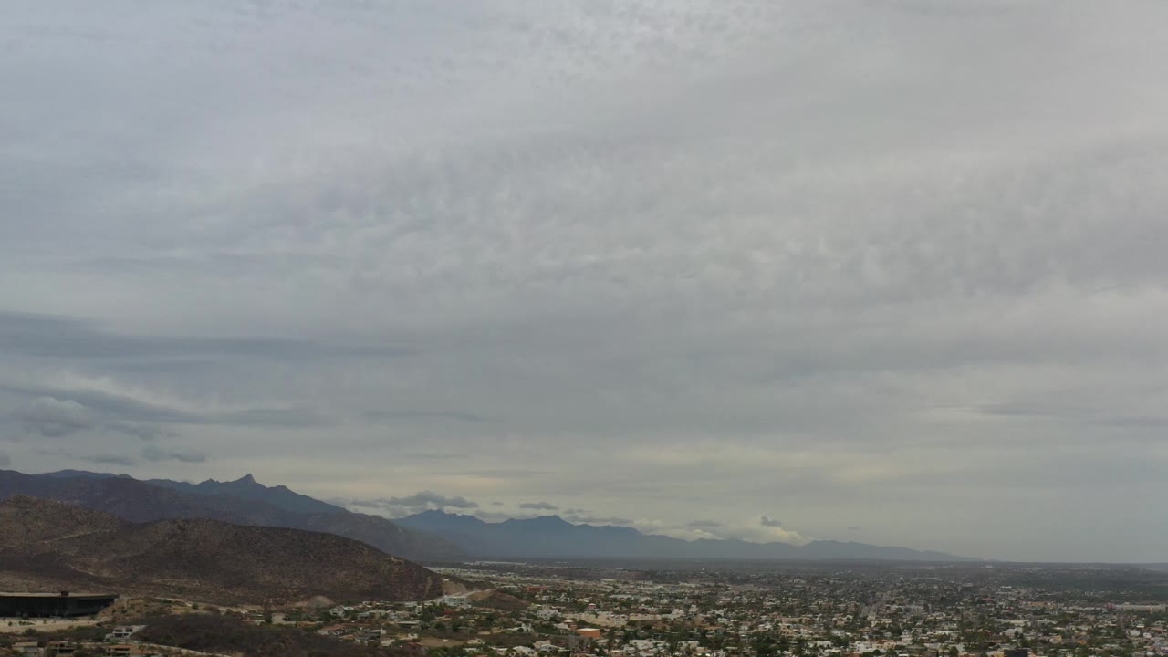 Wide city overlook beneath gray storm clouds and distant mountains.