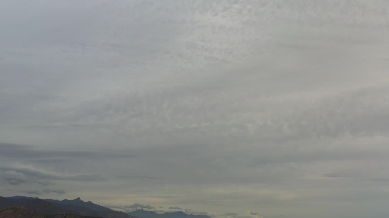 A wide Los Cabos, Mexico view shows layered gray clouds over dark distant mountains, with no visible people.