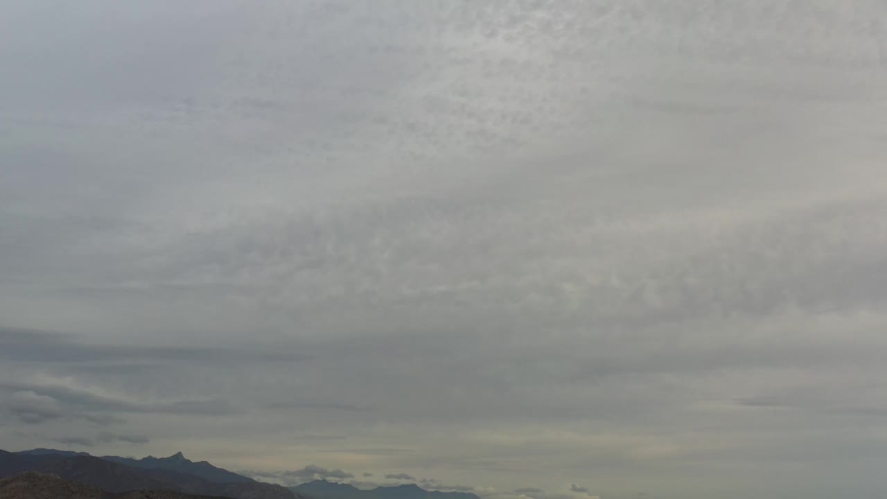 A sky-heavy Los Cabos frame holds soft gray cloud bands above a dark mountain silhouette, with no visible people.