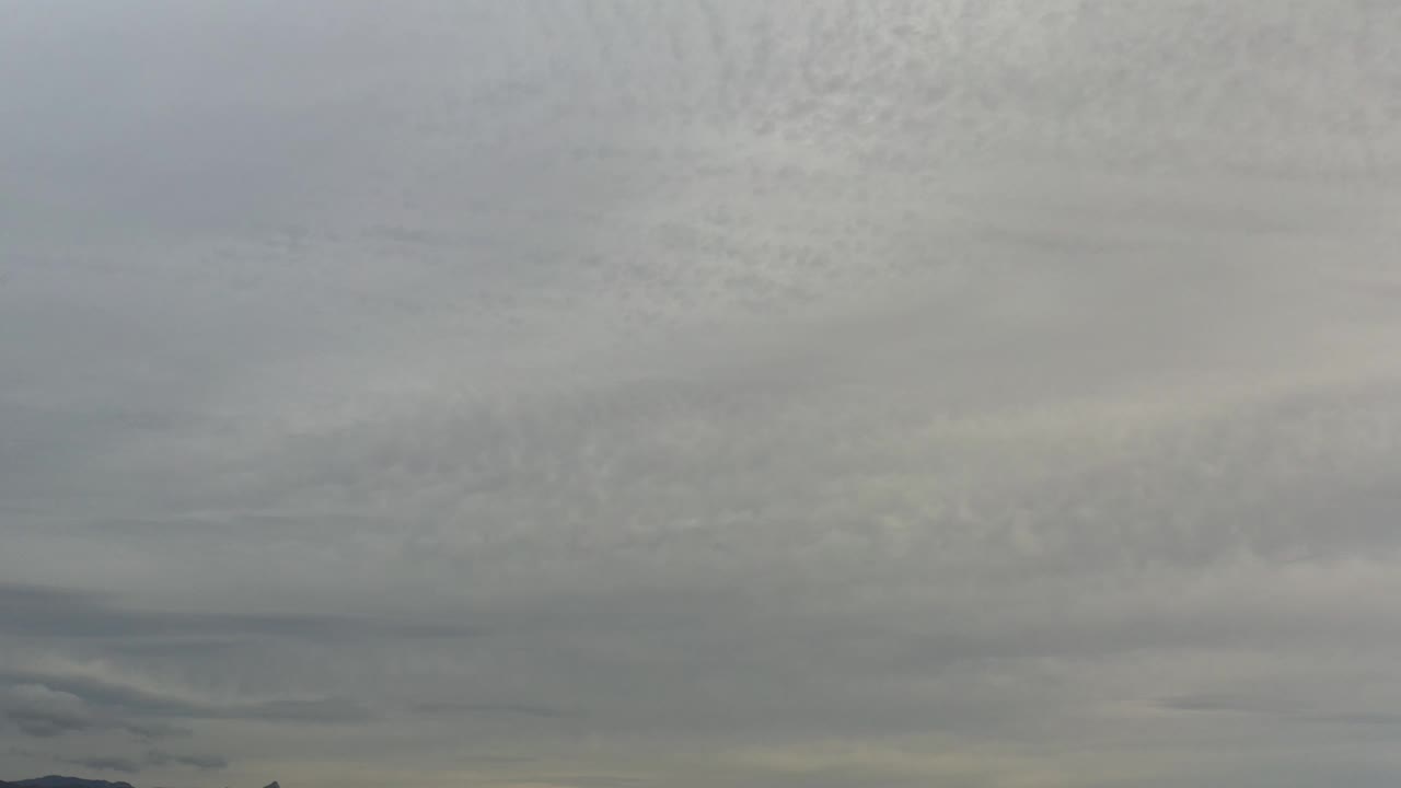 A dense gray cloud field hangs over Los Cabos with soft pale streaks near the lower edge and no visible people.