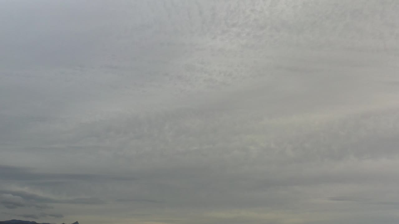 Layered gray and white stratus clouds fill the sky over a low dark horizon in Los Cabos, Mexico, with no visible people.