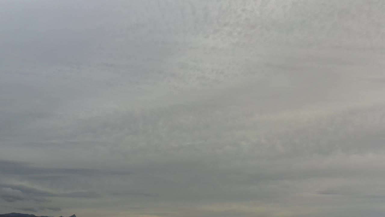 A broad overcast sky in Los Cabos, Mexico shows pale gray cloud layers stacked above a narrow distant horizon, with no visible people.