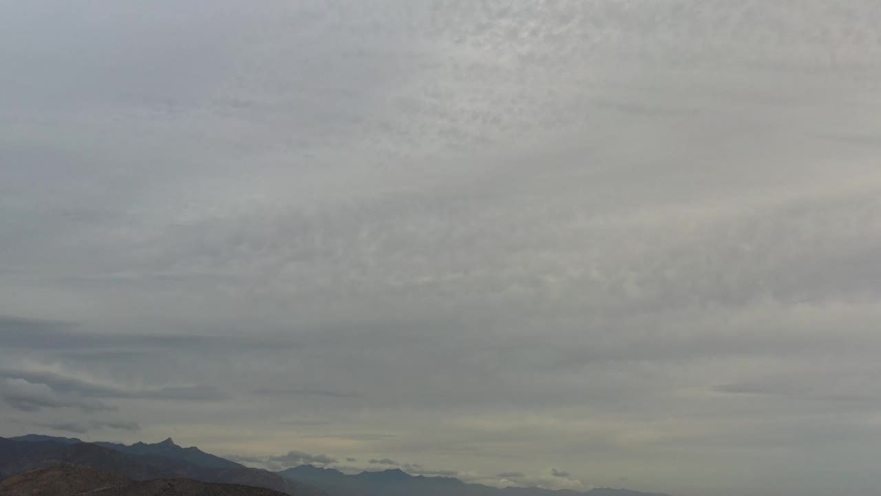 A broad Los Cabos cloud field hangs over dark mountain silhouettes and faint lighter ridges near the horizon, with no visible people.