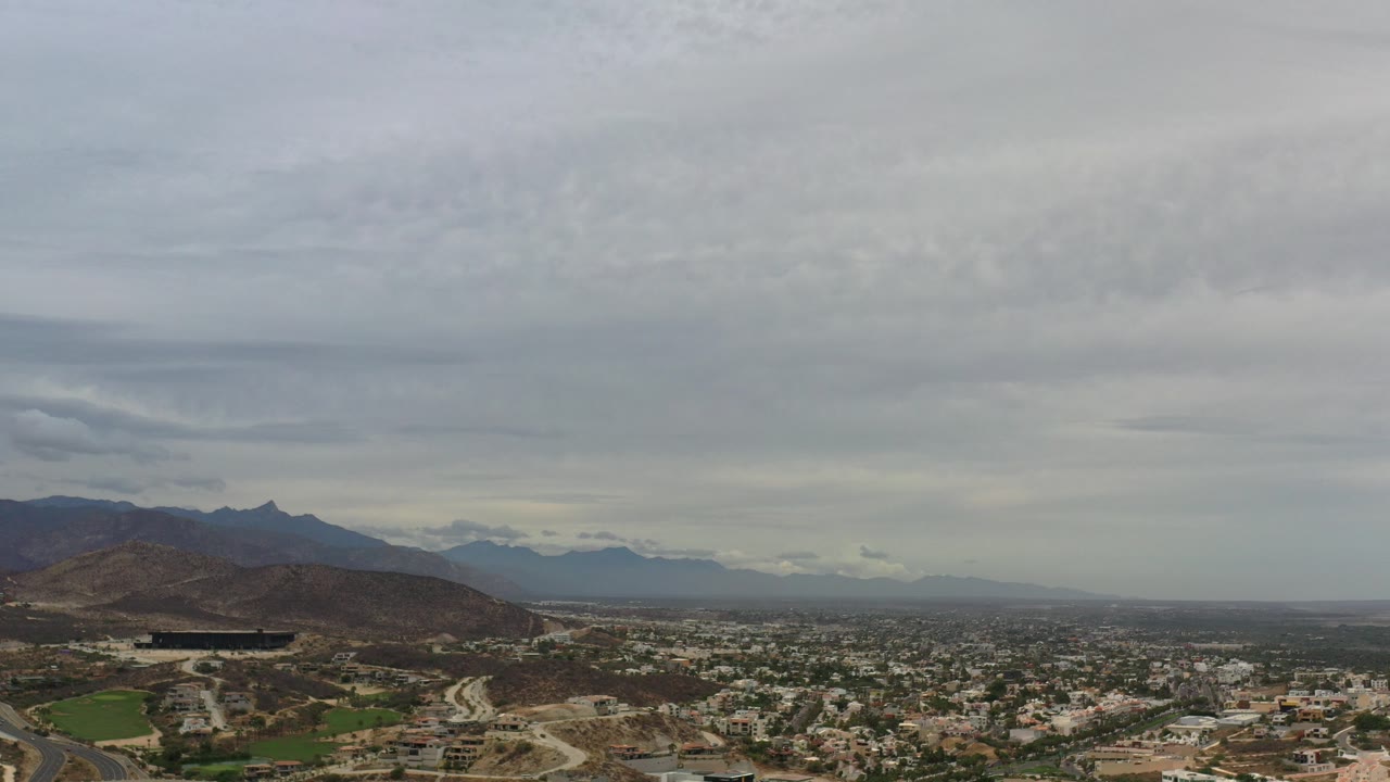 Wide aerial city view beneath gray stratus clouds and mountains.